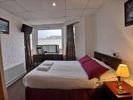Een hotelkamer met een bed, een bureau met een computer, een raam met gordijnen en een lampje op het nachtkastje.