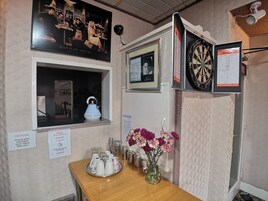 Een bar met een dartbord, een ingelijste foto en een menubord.