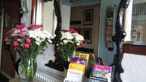 A reception desk with a vase of flowers, a mirror, and informational brochures. - The Hopton Hotel (Blackpool)