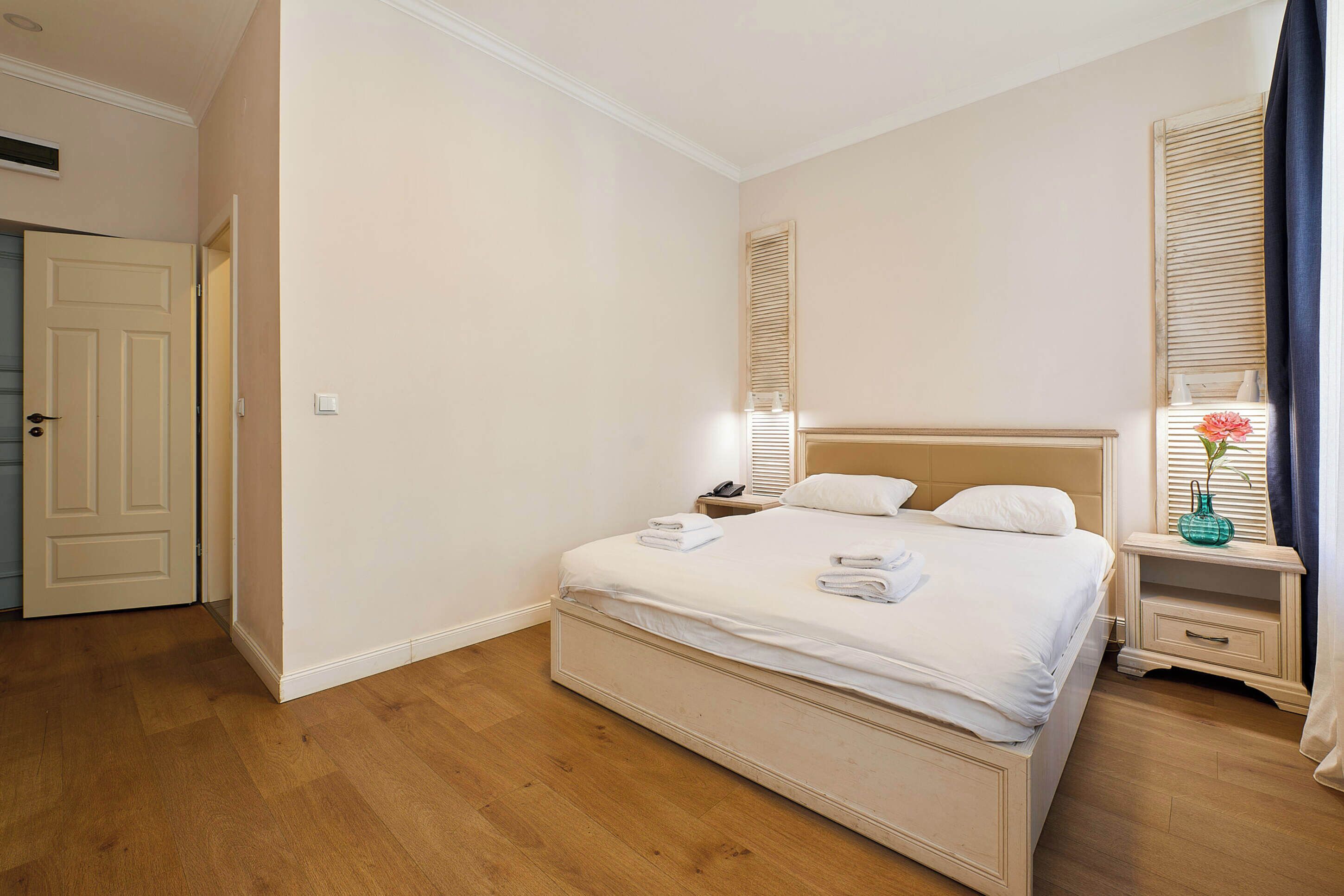 A bedroom with a large bed, a bedside table with a lamp, and a window with blinds.