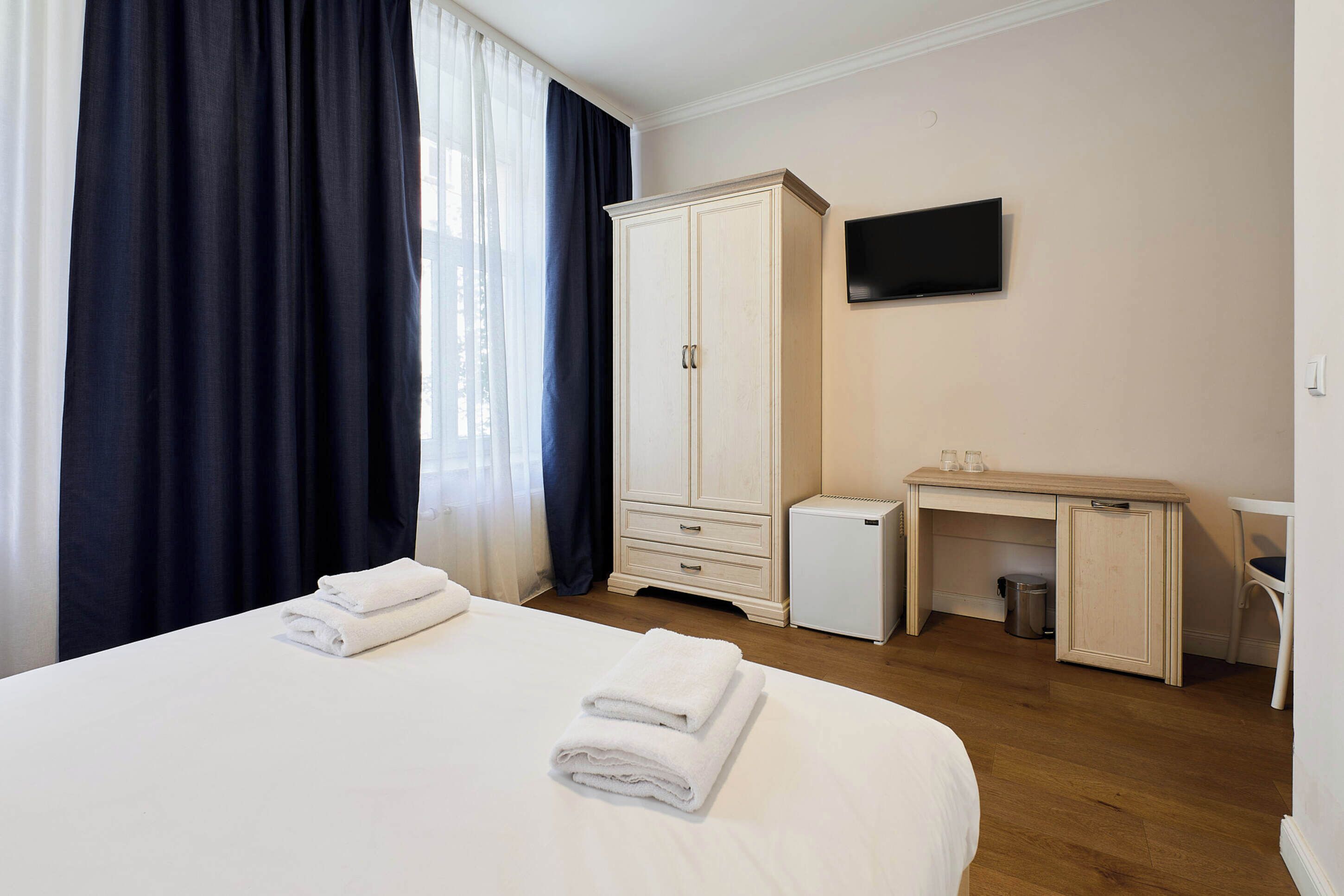 Una habitación de hotel con cama, escritorio, armario, televisor y un refrigerador pequeño.