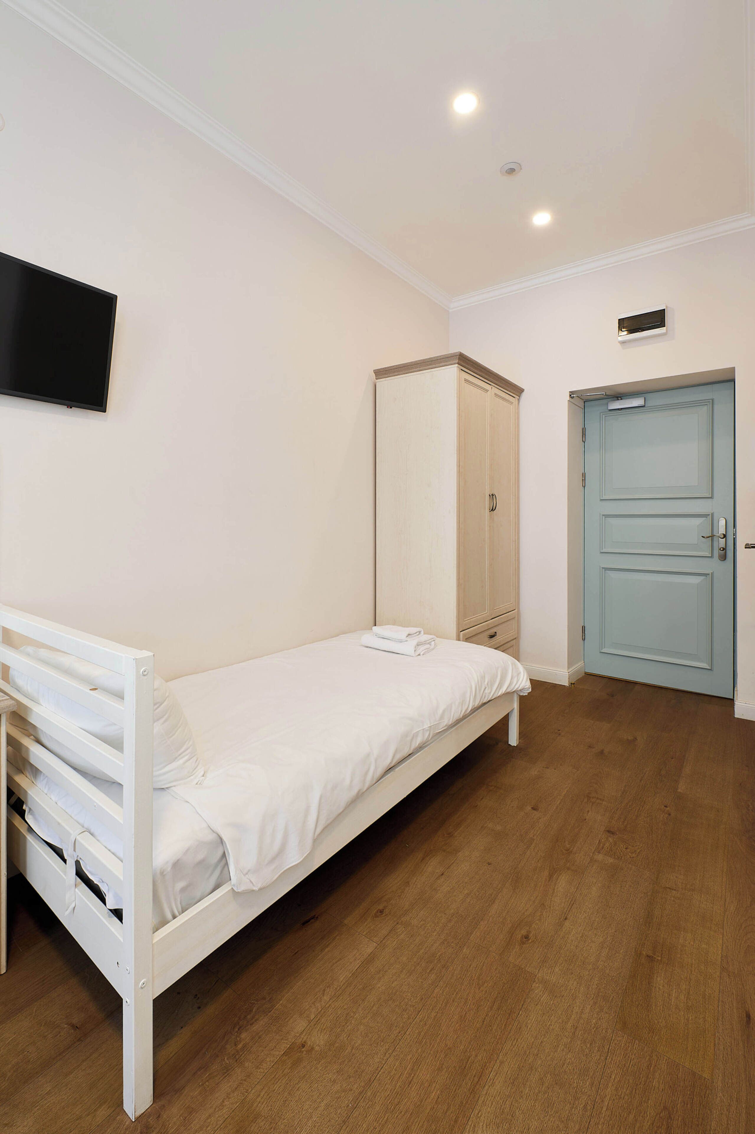 Habitación con una cama individual, suelo de madera, un armario, una puerta y un televisor de pantalla plana montado en la pared.