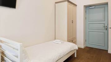 Habitación con una cama individual, suelo de madera, un armario, una puerta y un televisor de pantalla plana montado en la pared.