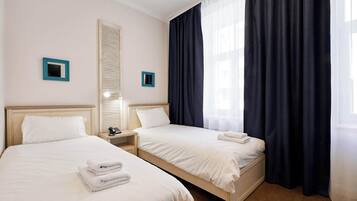 Une chambre d’hôtel avec deux lits, une table de chevet avec une lampe et une fenêtre avec des rideaux occultants.