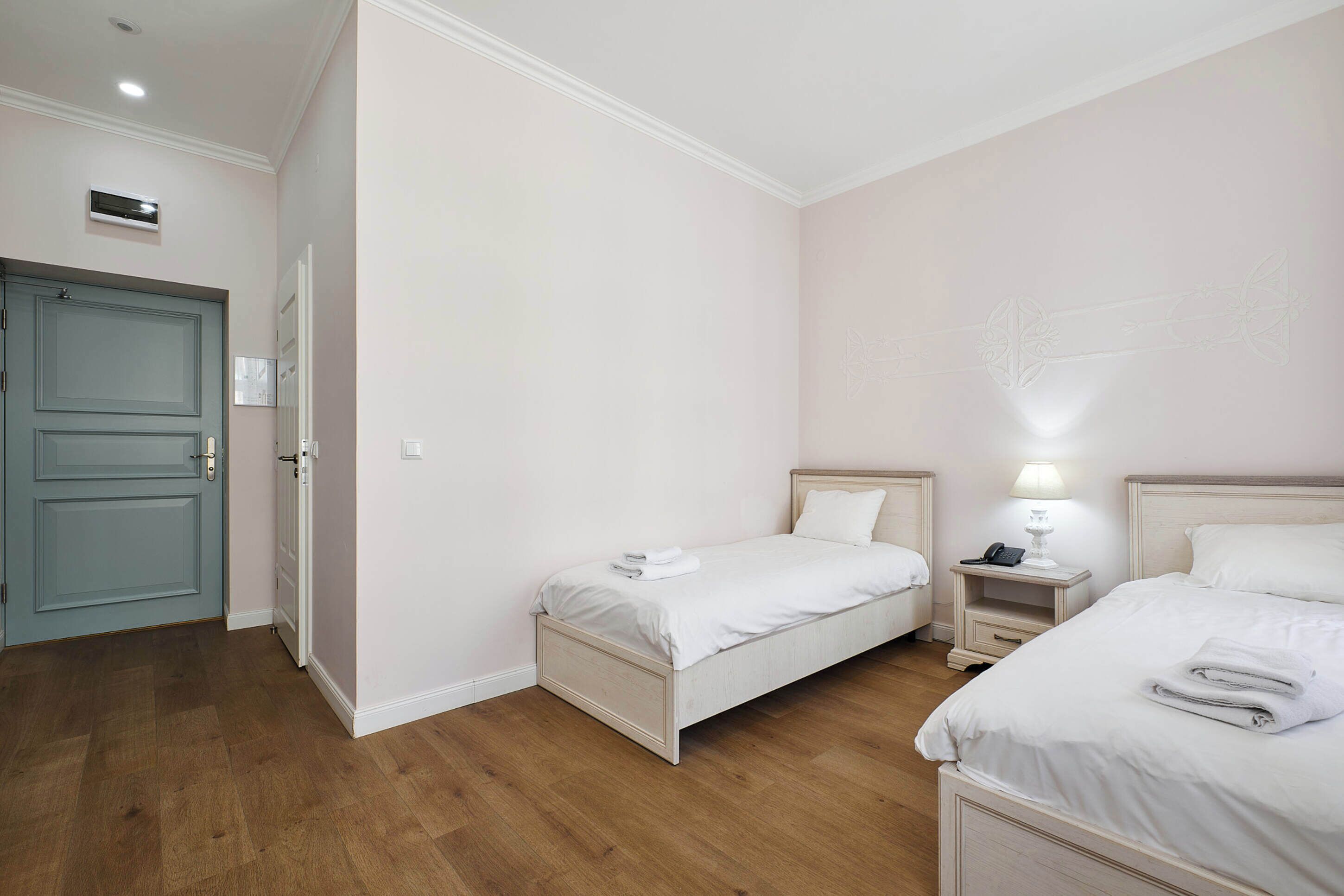 Een hotelkamer met twee eenpersoonsbedden, een nachtkastje met een lamp en een deur met lichtschakelaar.