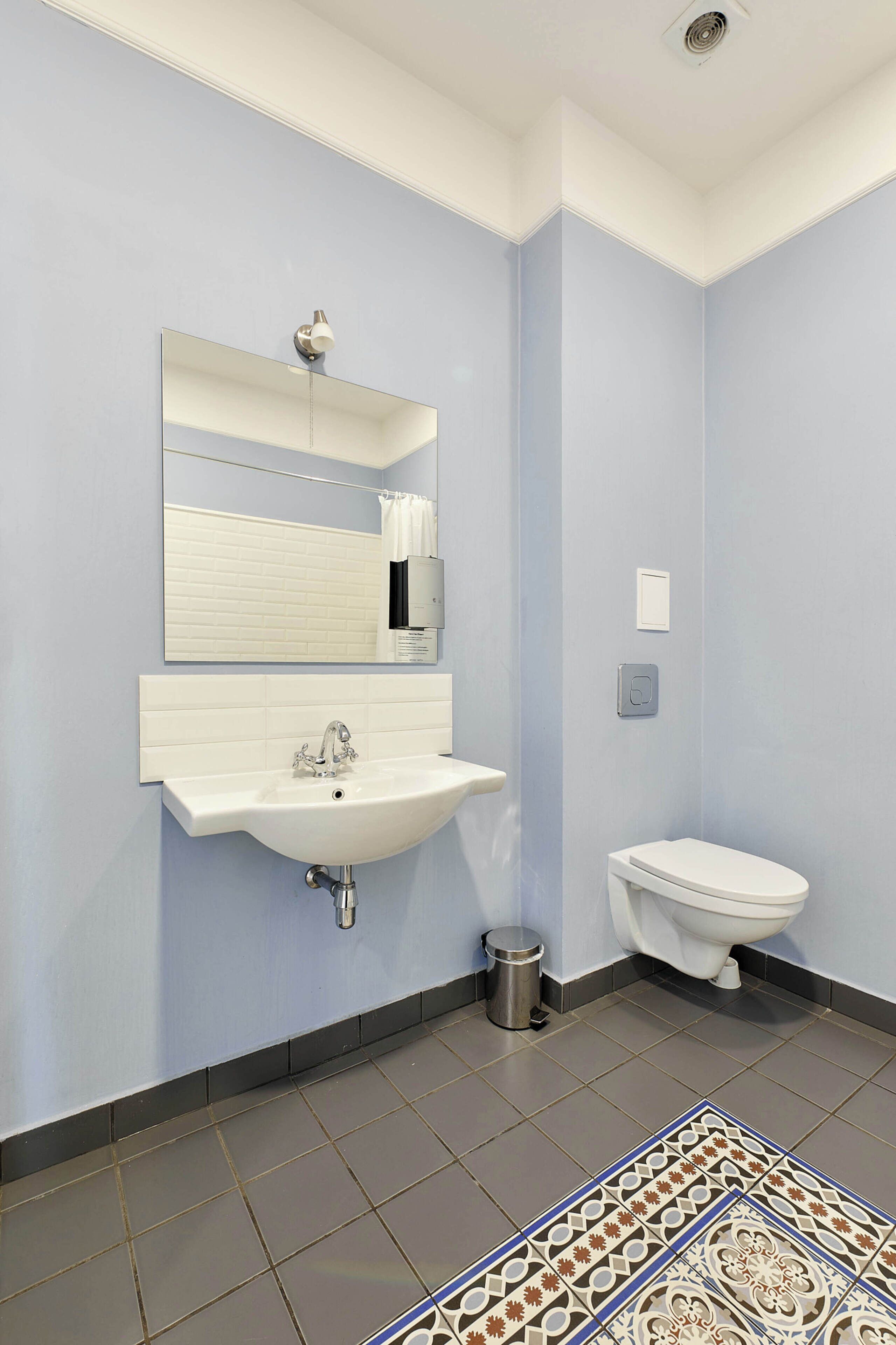Un baño con lavamanos blanco, un espejo, un inodoro y un cubo de basura.