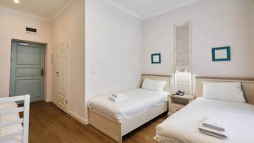 A hotel room with two single beds, a bedside table with a lamp, a small bedside table with a phone, and a door with a light switch.