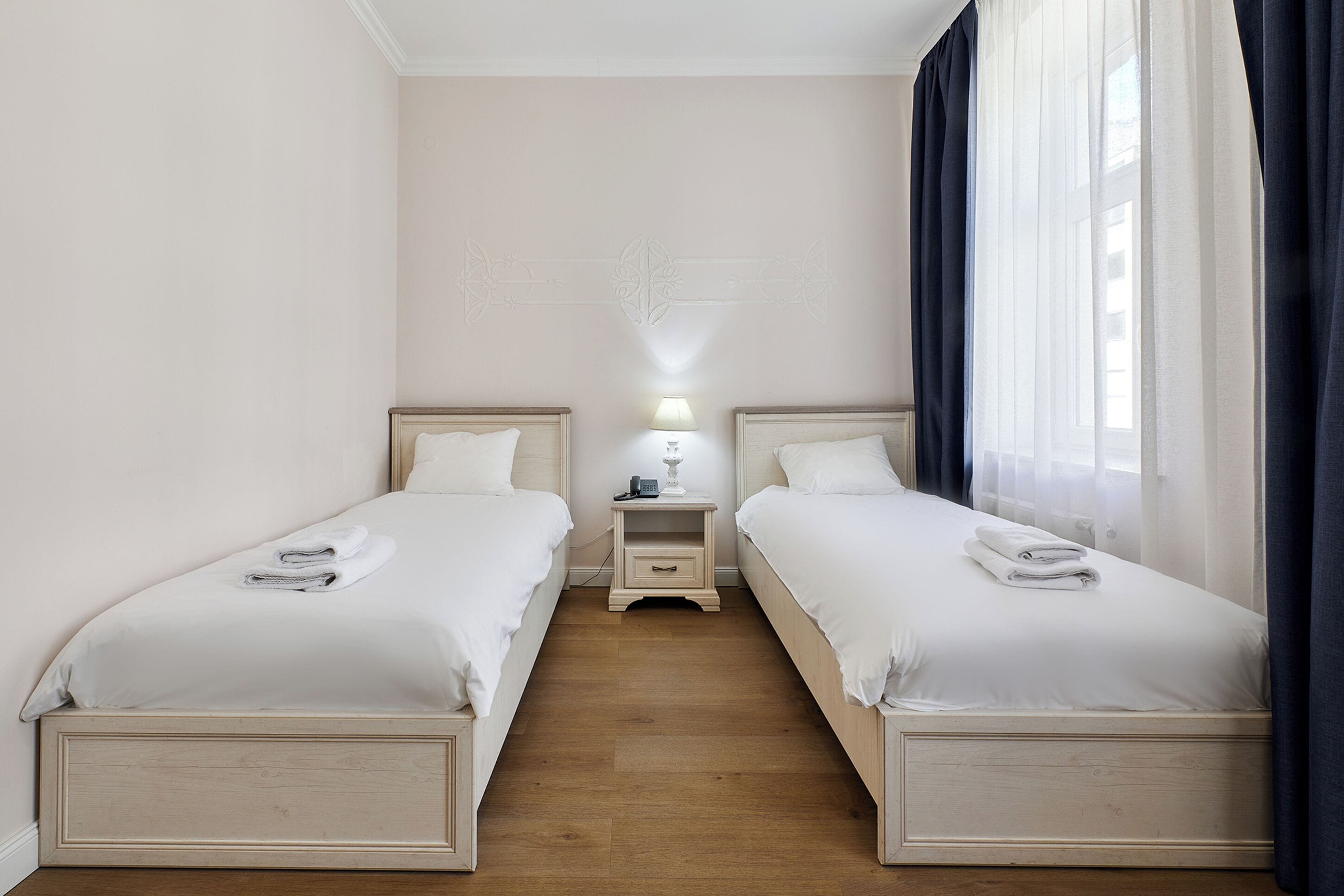 A twin room with two beds, a nightstand with a lamp, and a window with curtains.