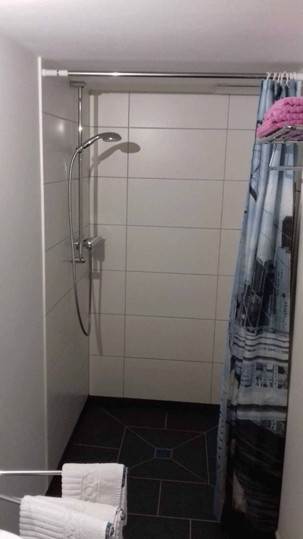 Um pequeno banheiro com revestimento de azulejos, chuveiro e cortina.