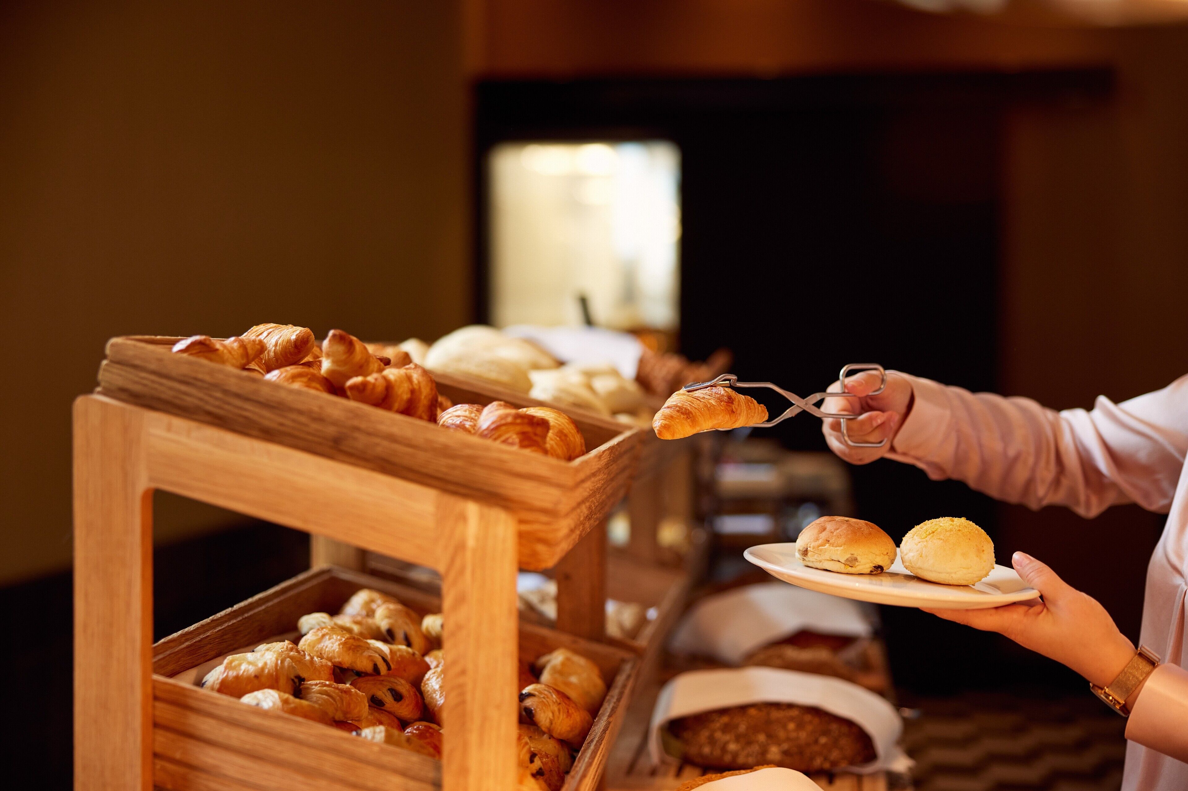 Buffet servindo diversos produtos de panificação, incluindo croissants e pães.