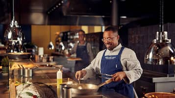 Un chef préparant des plats dans une cuisine professionnelle équipée d’appareils en acier inoxydable et éclairée par des lampes suspendues.