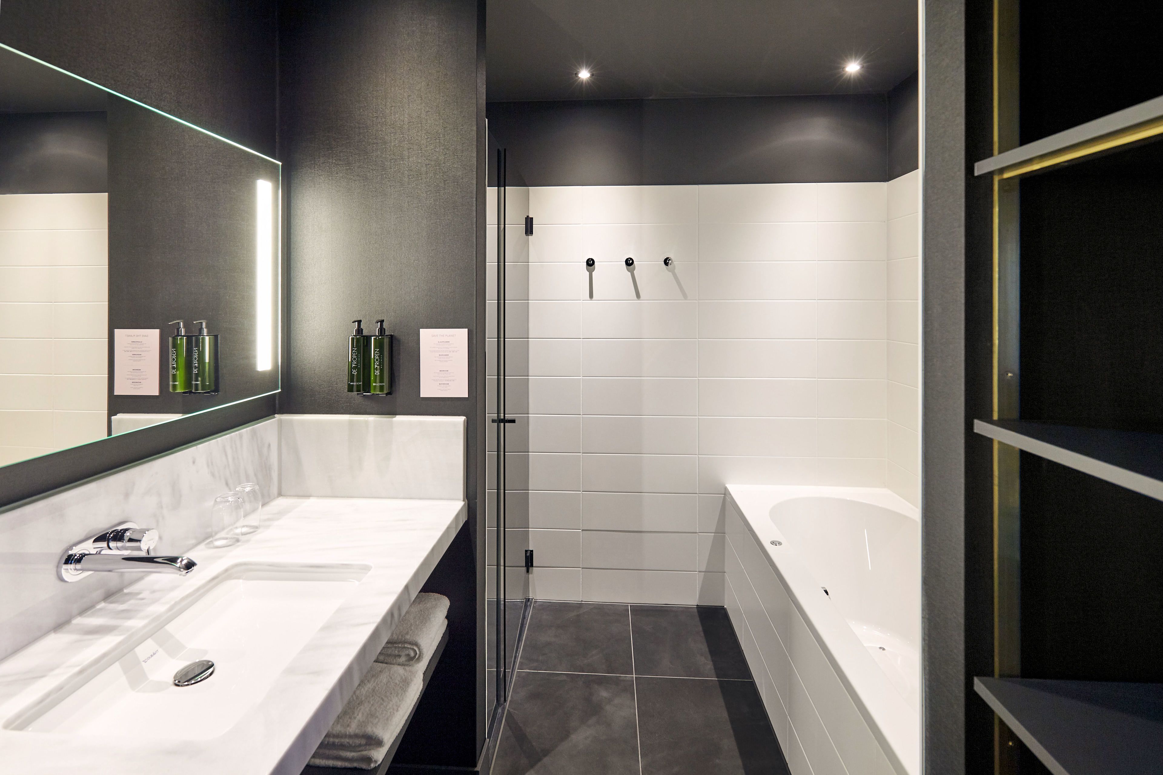 A modern bathroom with a large mirror, two sinks, a bathtub, and a shower area.