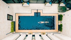 Ein rechteckiger Swimmingpool mit einer umlaufenden Holzterrasse, Stufen zum Wasser und Blick in den Himmel.