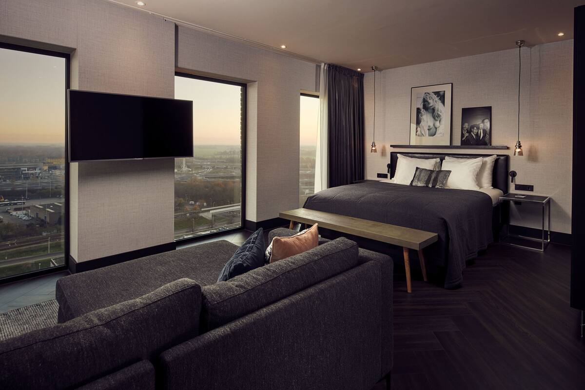 Una habitación de hotel moderna con una cama grande, un televisor de pantalla plana, un sofá y vistas a la ciudad.