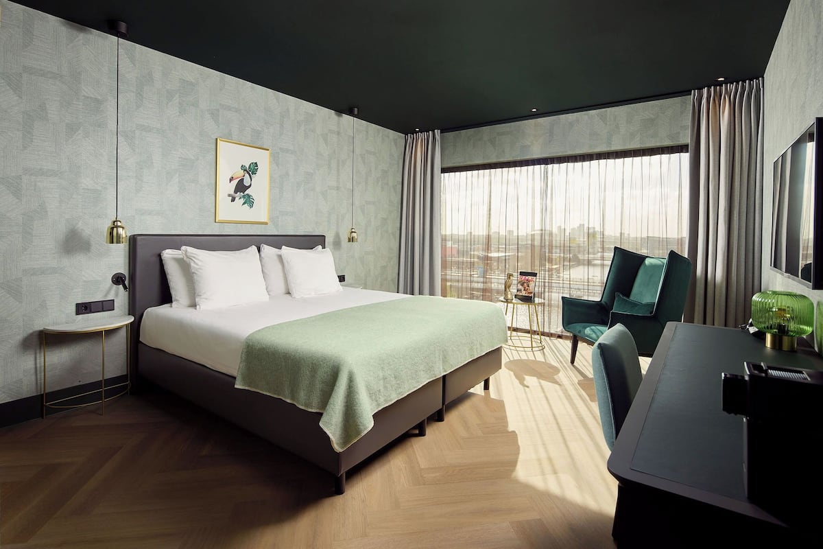 Una habitación de hotel moderna con una cama grande, un escritorio, una silla y vistas a la ciudad.
