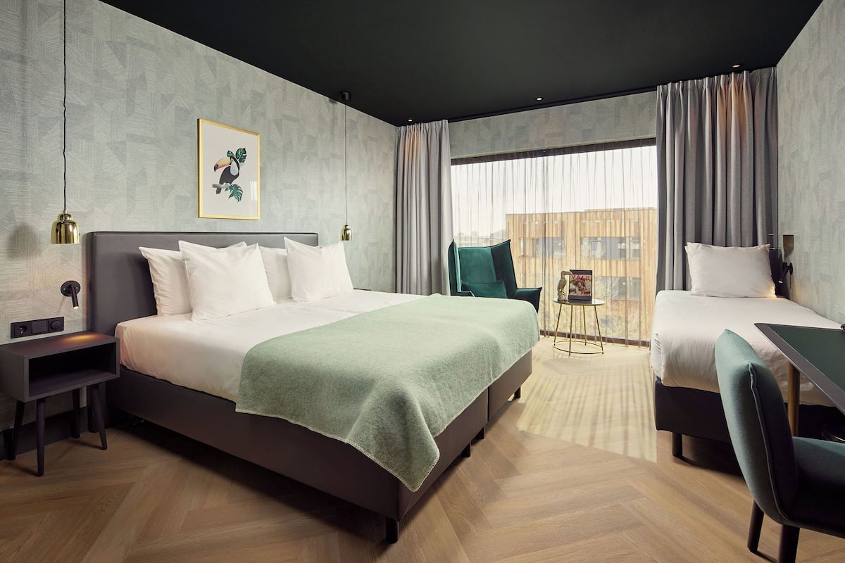 Una habitación de hotel moderna con una cama grande, una cama más pequeña, un escritorio y una silla.