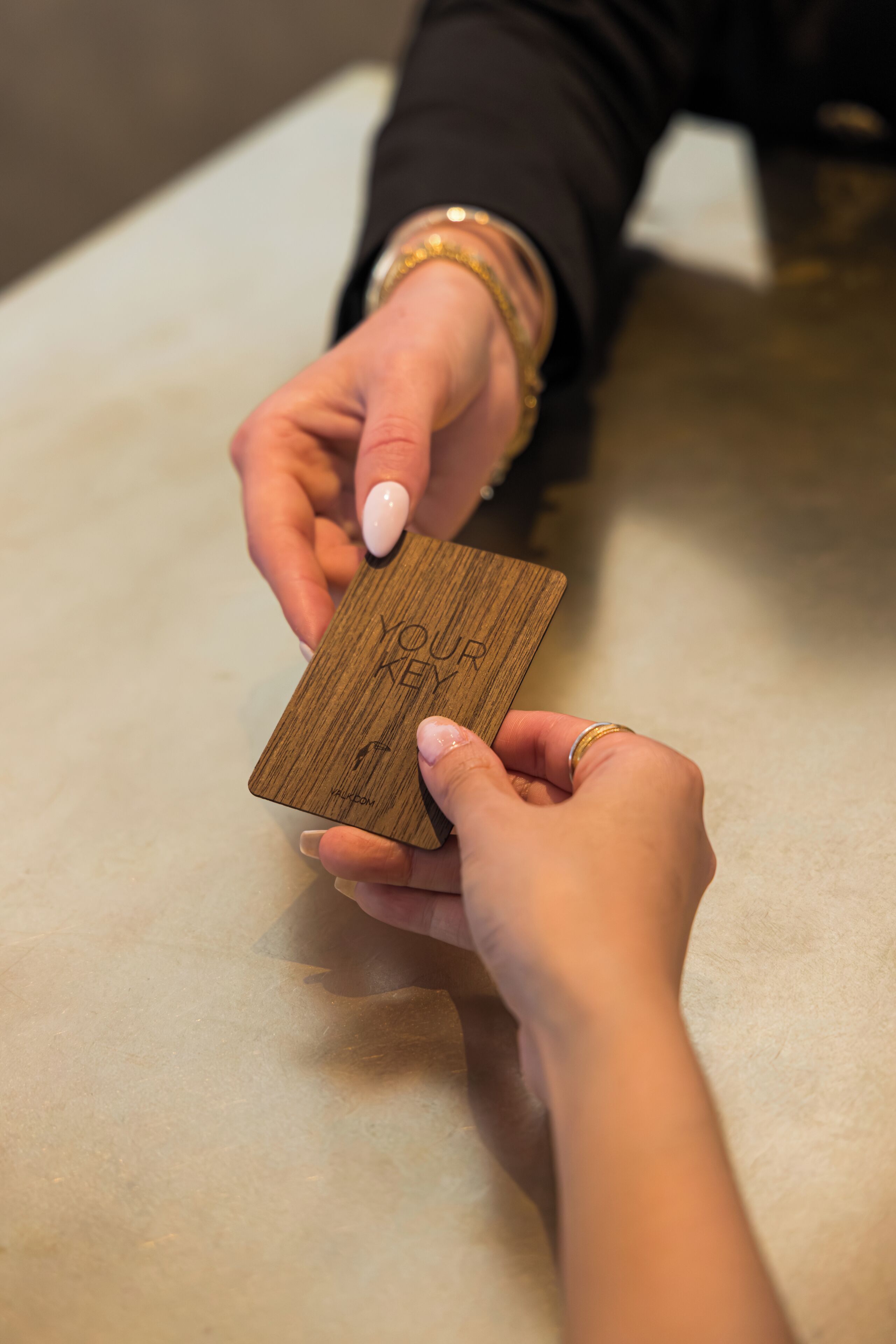 Una persona sostiene una tarjeta de madera con el texto 'YOU ARE KEY' y 'WELCOME'.