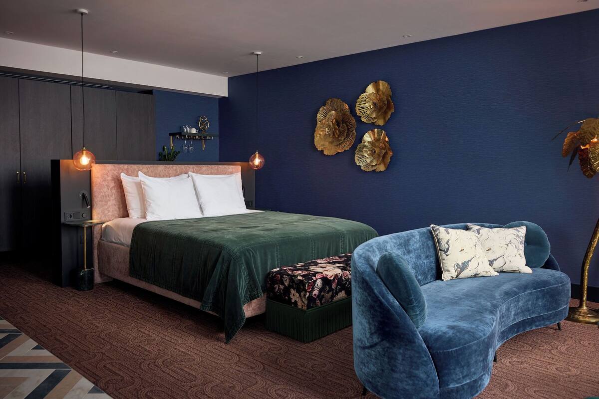 Un dormitorio moderno con una cama, un sillón azul, una mesita de noche y detalles decorativos en la pared.
