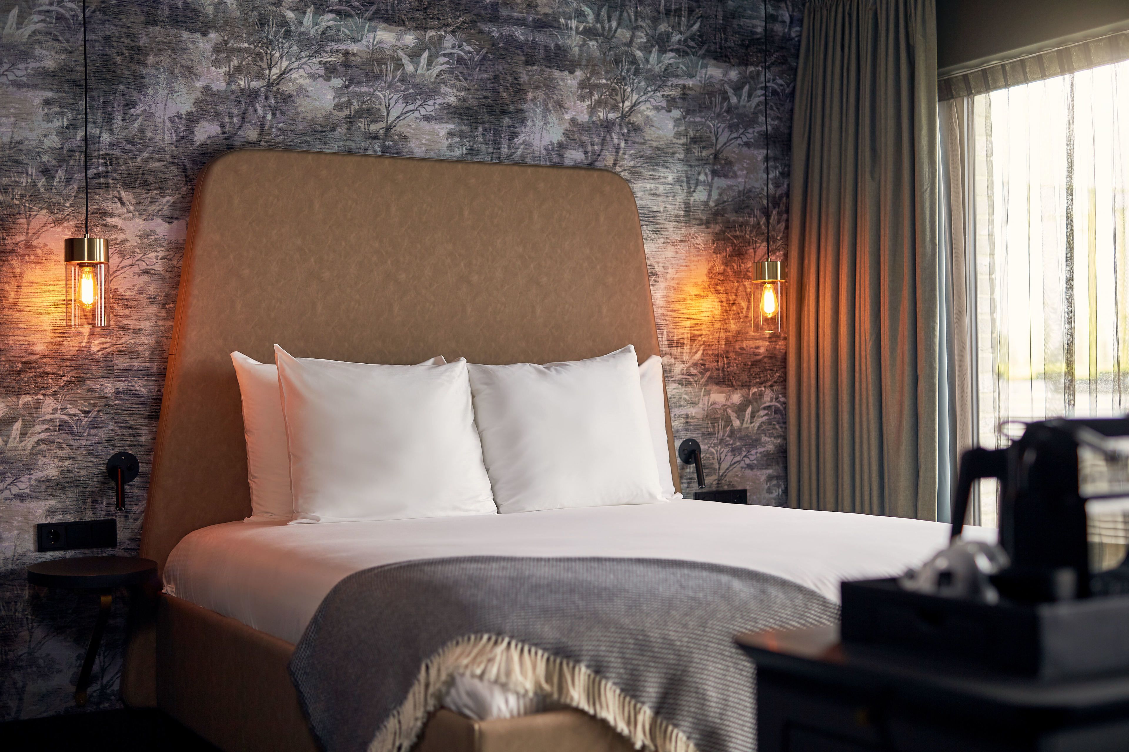Una cama bien hecha con sábanas blancas y un cabecero color beige en una habitación con pared texturizada y dos lámparas de pared.