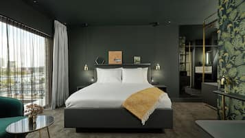 Een moderne hotelkamer met een groot bed, een klein tafeltje, een stoel en uitzicht op de stad door grote ramen.