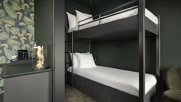 Una cama individual superpuesta con escritorio y silla, un objeto en forma de cúpula de vidrio, y una pared con diseño de hojas.