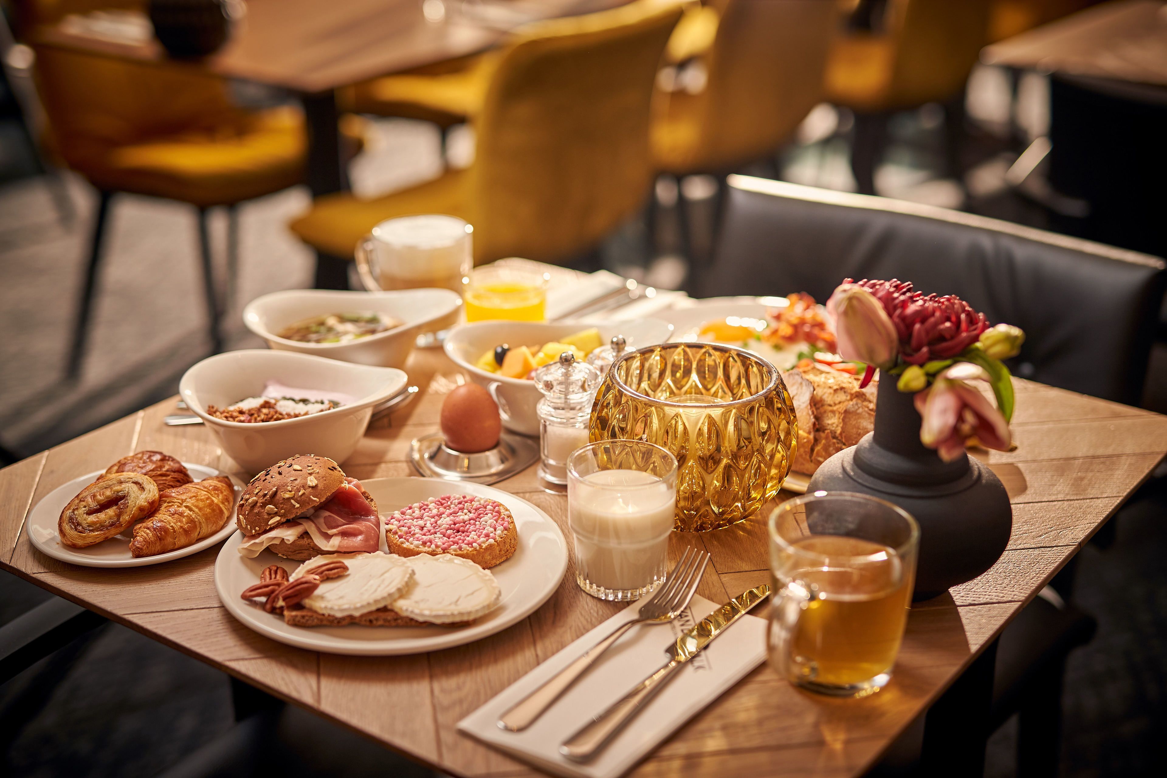Un desayuno con diferentes platillos, como pastelería, frutas y un jarrón decorativo.