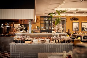 Een restaurant interieur met een bar, een keuken op de achtergrond en diverse eettafels met stoelen.