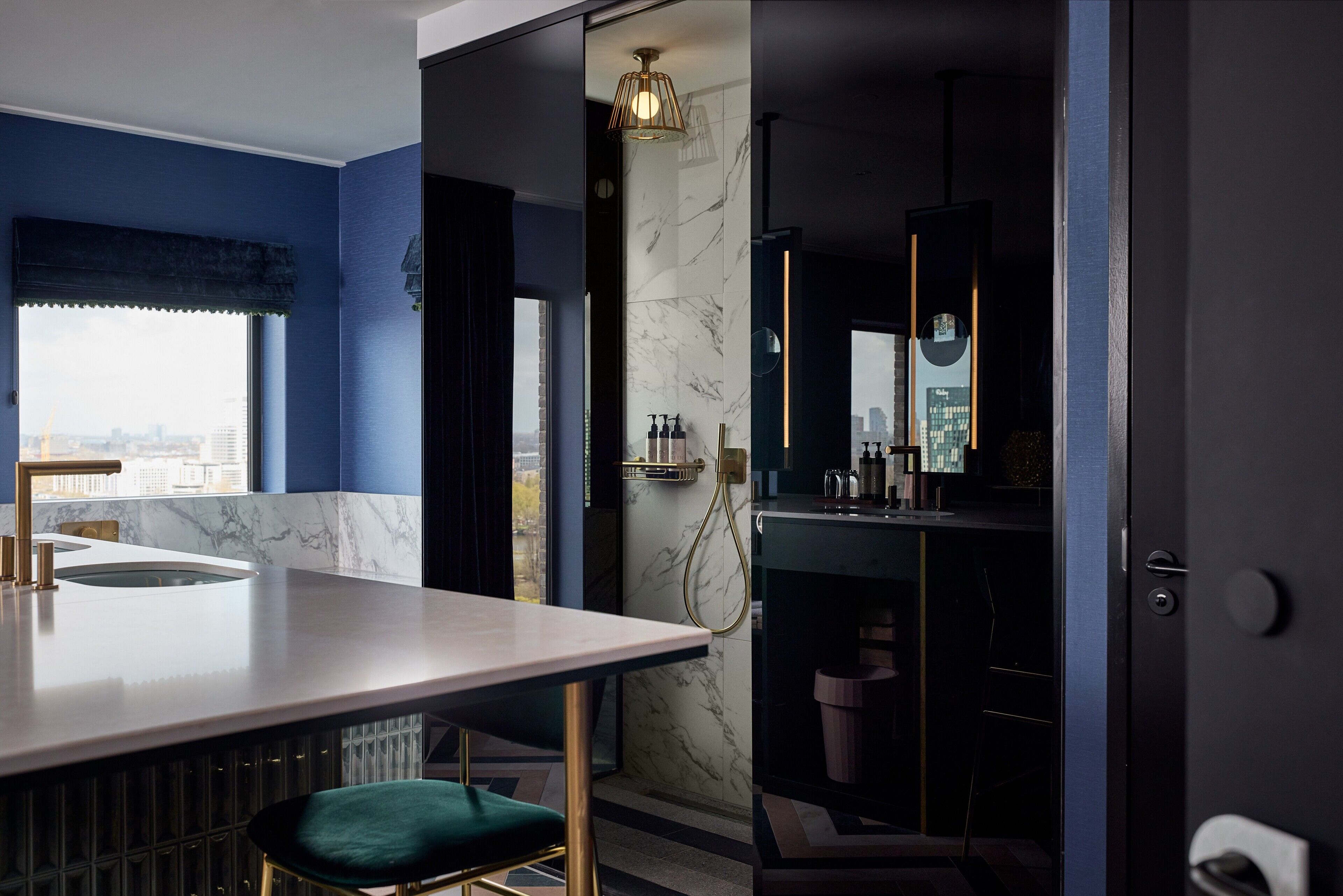 A modern bathroom with a marble wall, a gold shower head, and a view of the city.