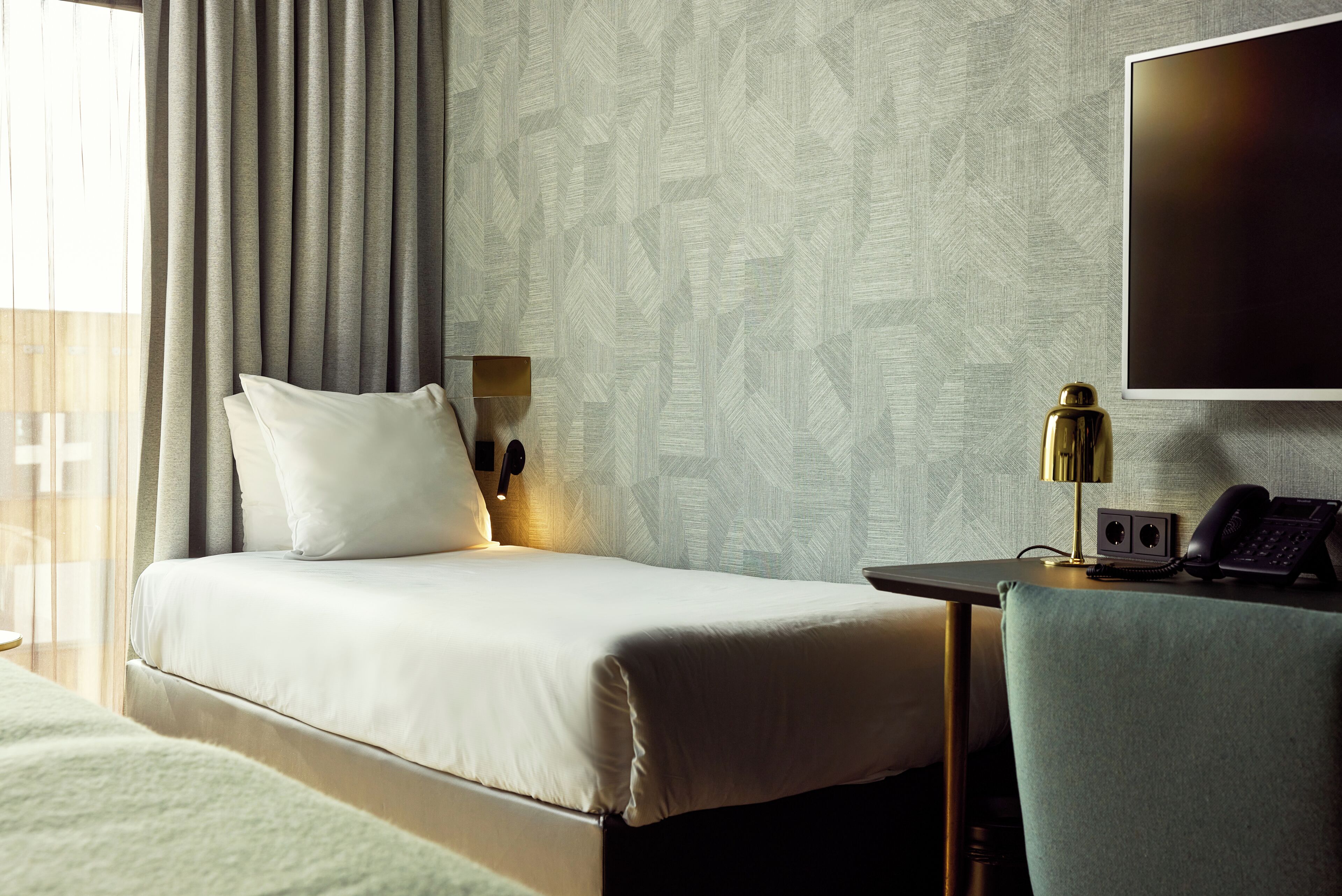 Ein Hotelzimmer mit Bett, Schreibtisch mit Lampe, Telefon und Fernseher.