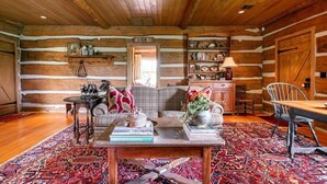 A log cabin interior with a cozy seating area, a dining table, and a bookshelf.