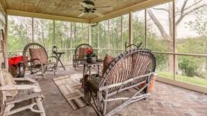 A covered porch with wicker furniture, a ceiling fan, and a view of trees.