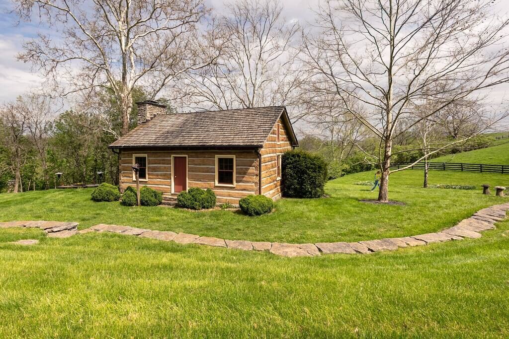 A small log cabin with a red door, surrounded by a well-maintained lawn and a stone pathway.