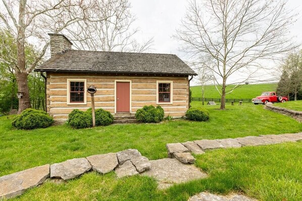 A log cabin with a red door, surrounded by a stone pathway and green grass. - Cabin in Kentucky Horse Country (Bourbon County)