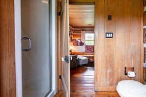 A wooden interior with a visible bathroom, a bed with pillows, and a small seating area. - Cabin in Kentucky Horse Country (Bourbon County)