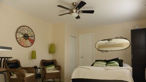 A bedroom with a bed, two wicker chairs, a green rug, a wall clock, a ceiling fan, a mirror, and a door. - Dream holiday at a low price: huge travel discounts now available! (Cape Coral)
