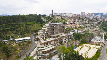 A multi-story hotel with a modern design, located in a hilly area with surrounding greenery and residential buildings.