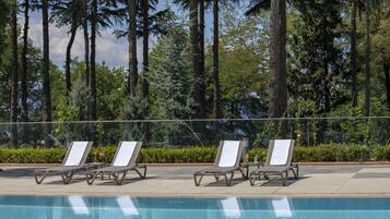 Zona de piscina con sillas de descanso y vista a árboles altos.