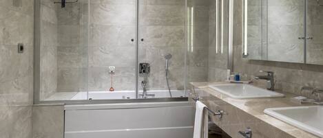 A modern bathroom with a large bathtub, two sinks, and a glass-enclosed shower.