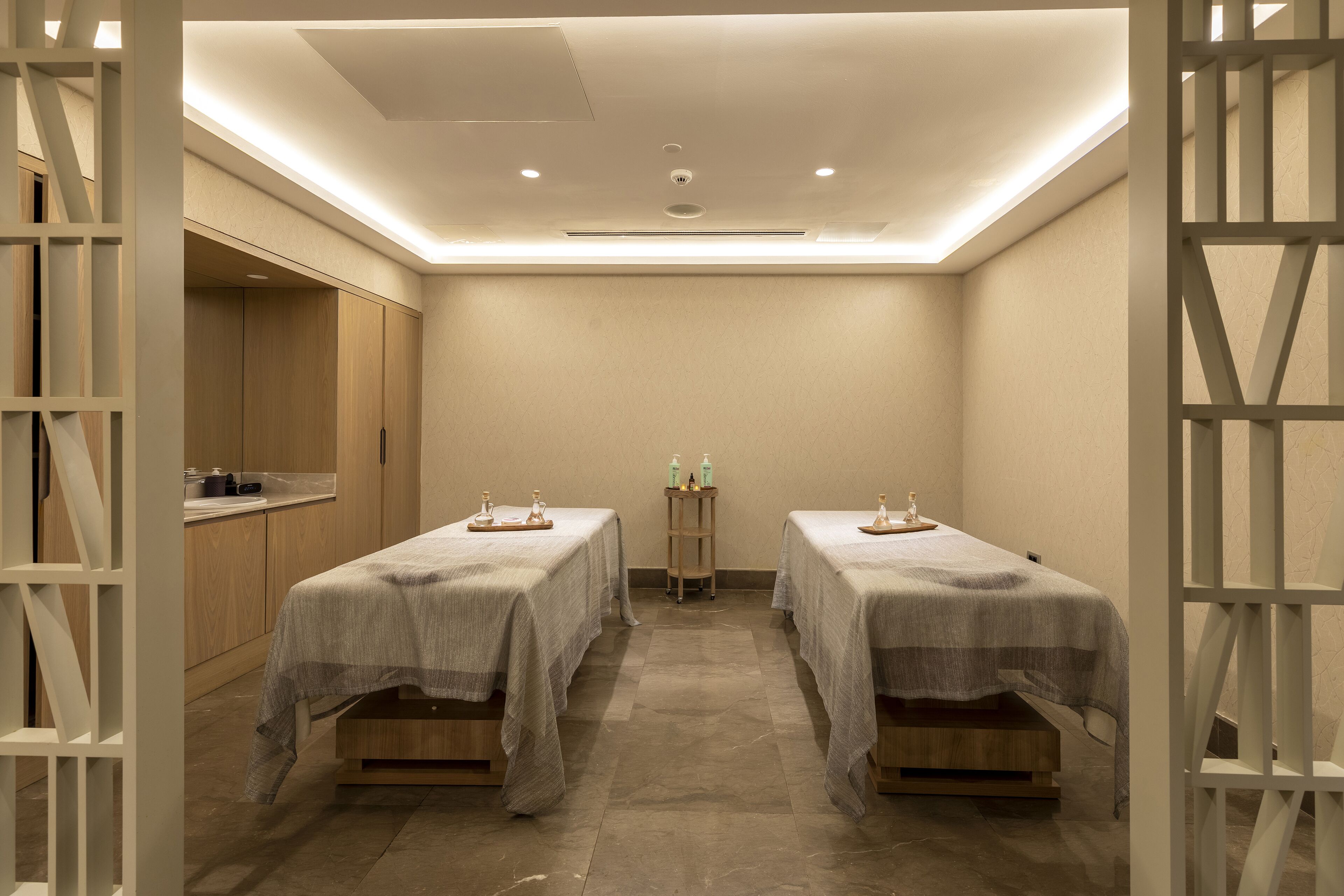 A room with two beds, a small table with toiletries, and a kitchenette area.