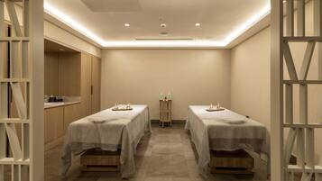 A room with two beds, a small table with toiletries, and a kitchenette area.