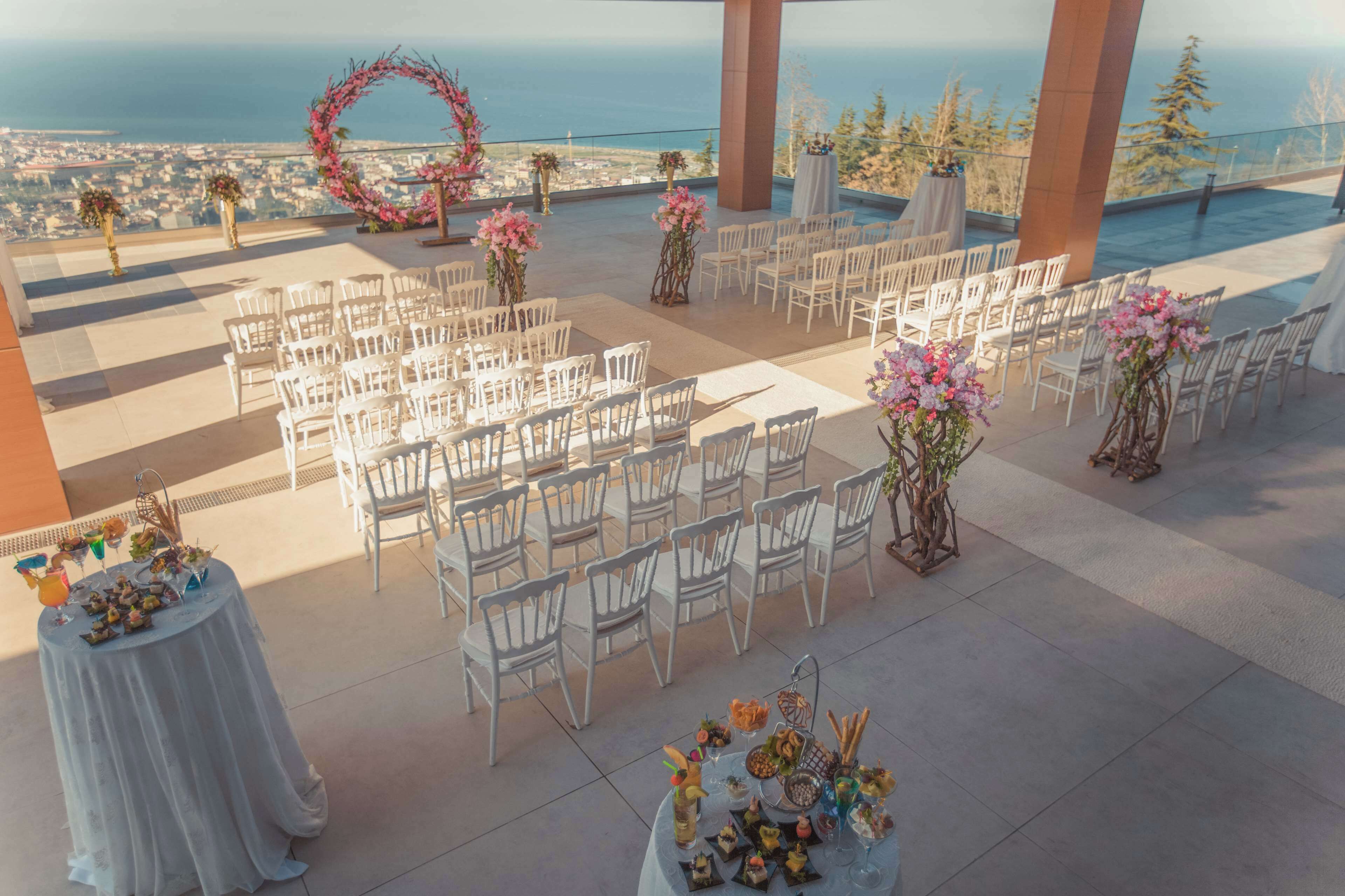 Un lugar para bodas al aire libre con sillas blancas dispuestas en filas, decoraciones florales y vistas al océano.