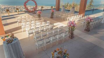 Un lugar para bodas al aire libre con sillas blancas dispuestas en filas, decoraciones florales y vistas al océano.