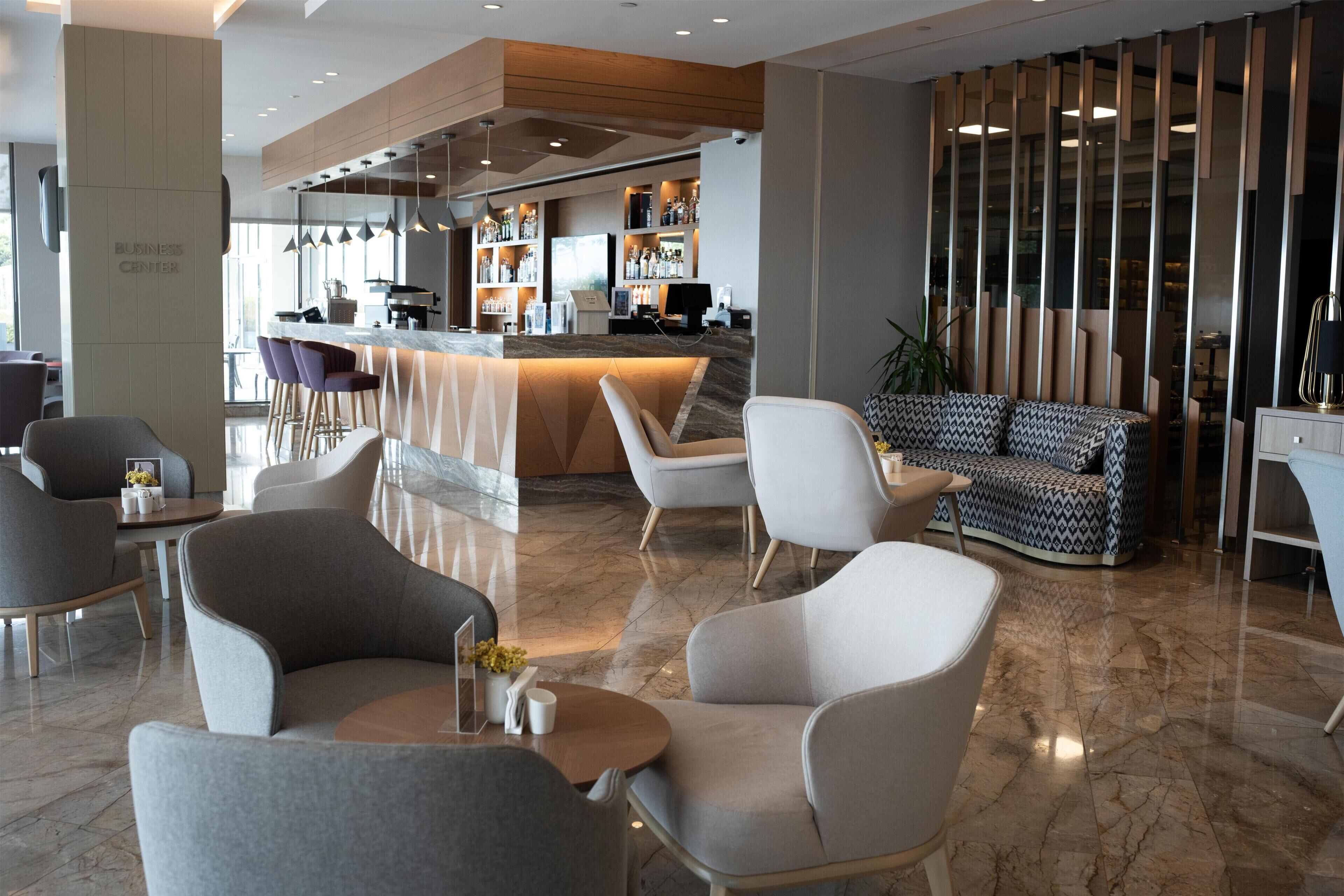 Um saguão moderno de hotel com área de bar, assentos e balcão de recepção.