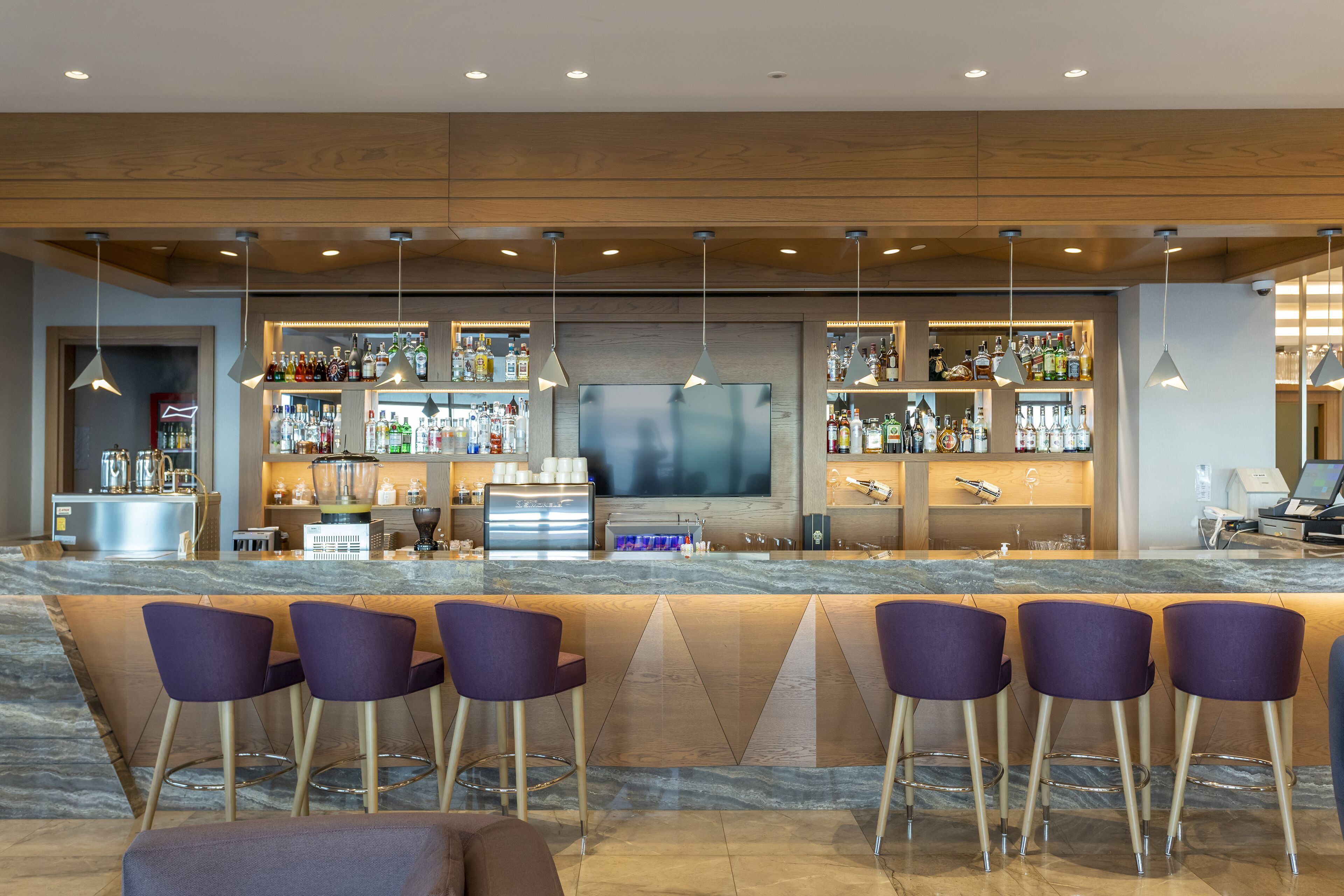 Een moderne bar met een marmeren aanrecht, barstoelen en een grote flatscreen televisie.