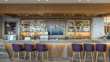 Een moderne bar met een marmeren aanrecht, barstoelen en een grote flatscreen televisie.