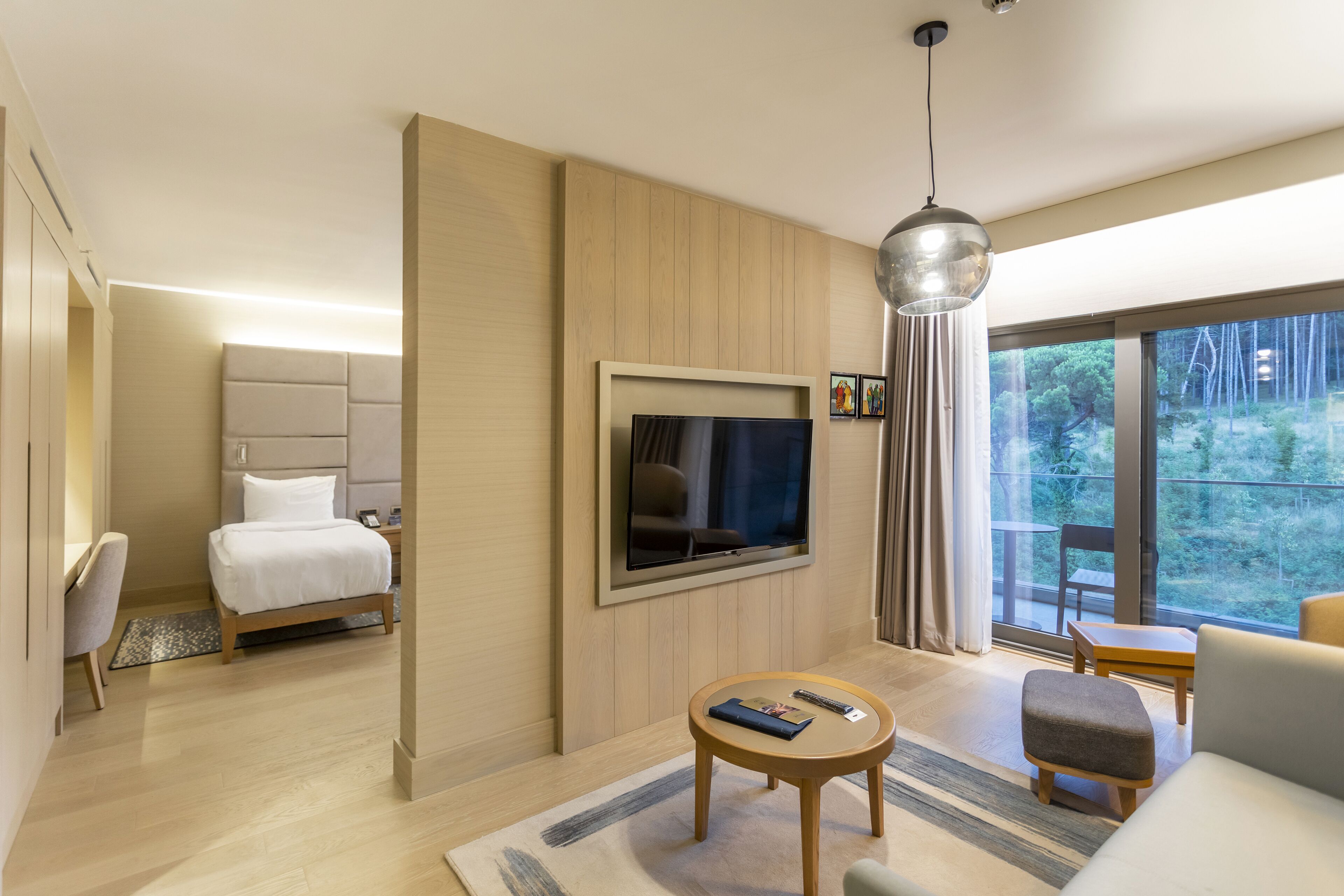 Habitación de hotel moderna con cama, televisión, sofá, mesita pequeña y vistas al exterior.