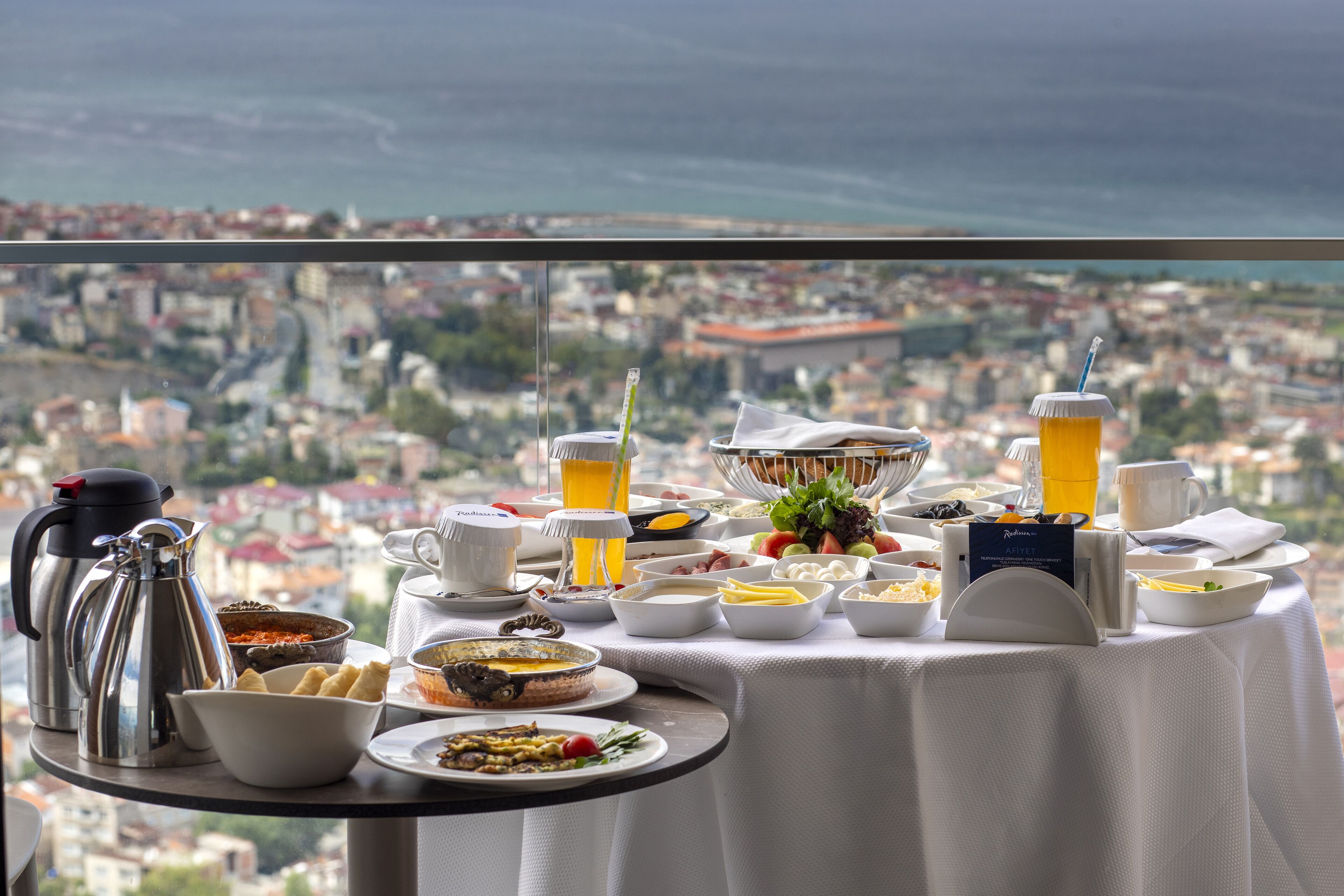 Ein Frühstücksbuffet mit vielfältigen Speisen und Getränken, vor der Kulisse einer Stadtlandschaft und des Meeres.