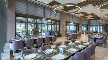 Un comedor amplio con varias mesas dispuestas para comer, ventanas grandes que ofrecen vistas y un diseño de techo moderno.