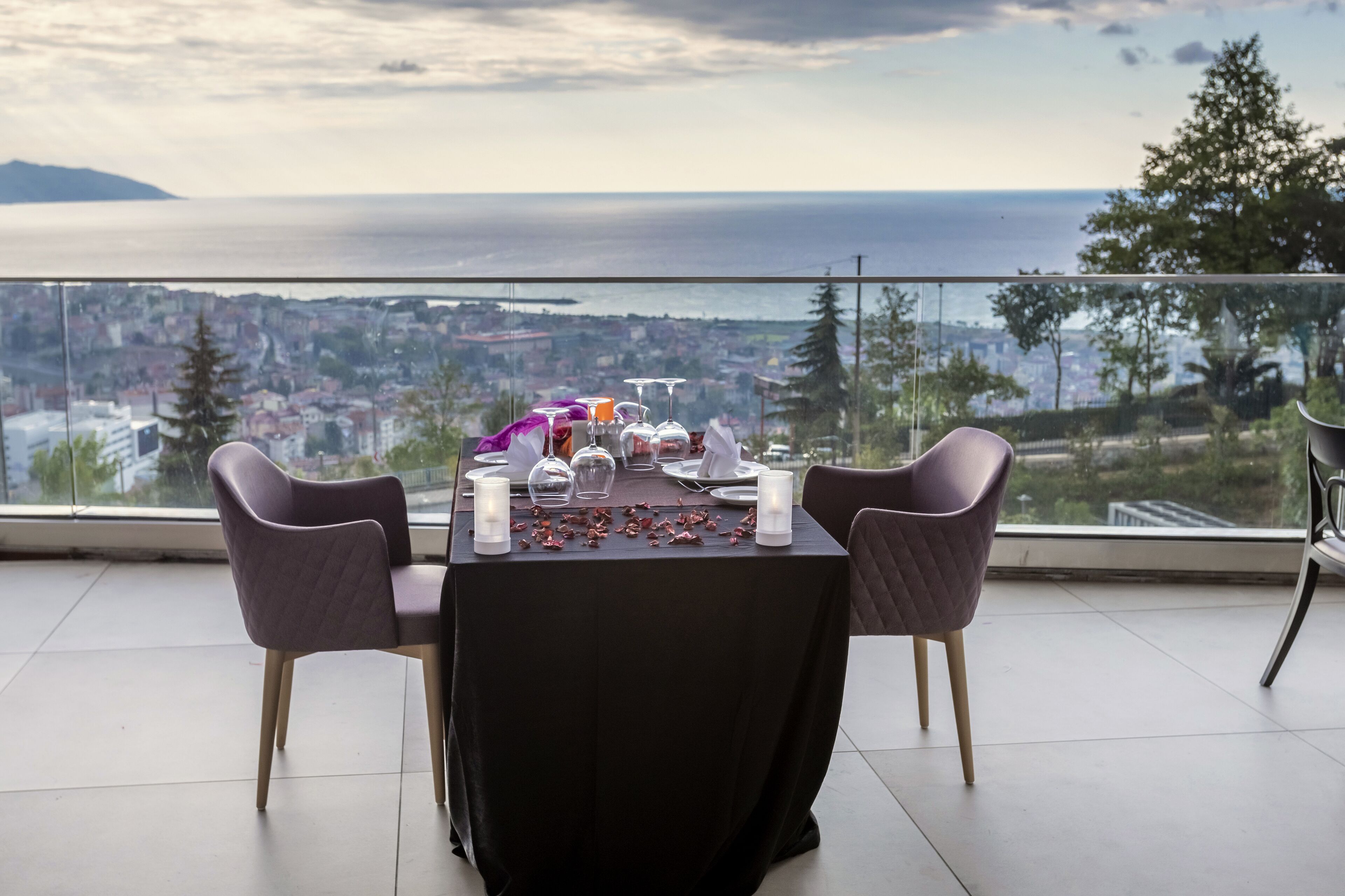 A dining table set for two with a view of the city and sea.