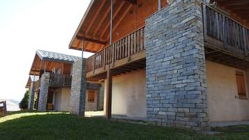 Un bâtiment à deux étages, doté d’une façade en pierre, de balcons en bois et d’un espace extérieur abrité.